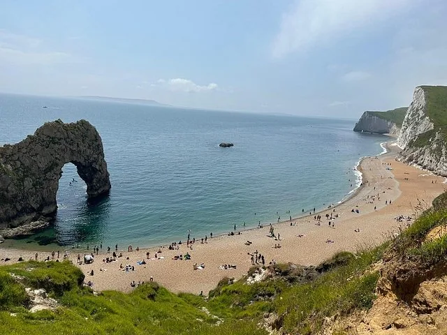 Vue panoramique de l'arche de Durdle Door et de la plage, avec des personnes dispersées autour