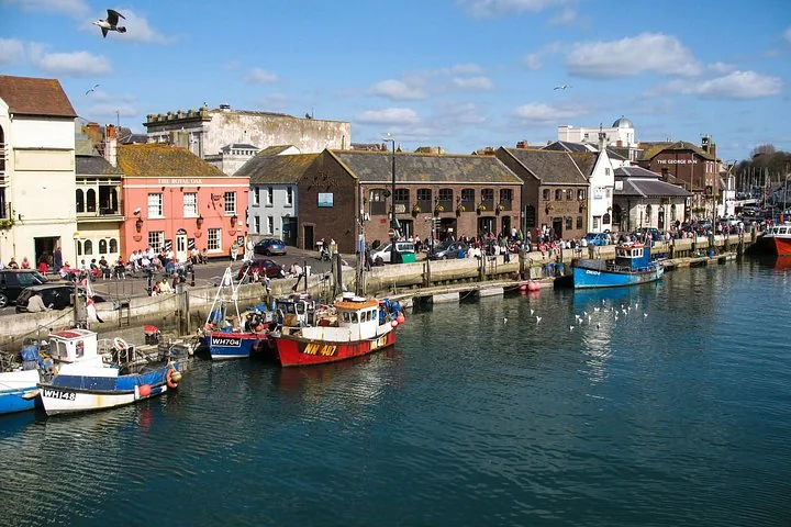 Harbor scene with colorful boats, waterfront buildings, and a bright blue sky.